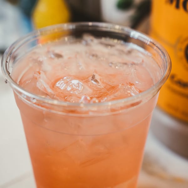 Close-up of a refreshing pink drink with ice in a clear plastic cup.