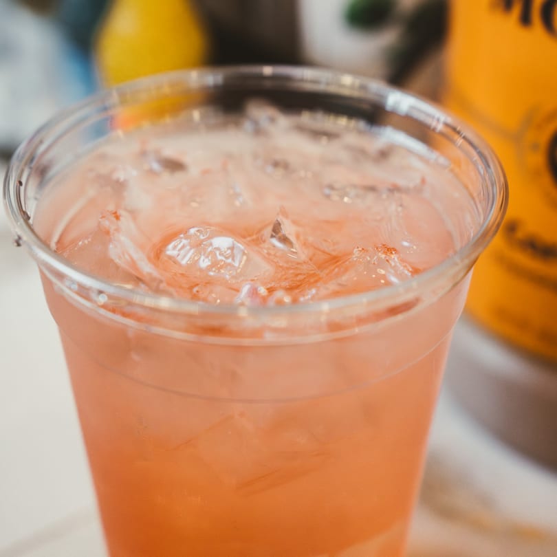Close-up of a refreshing pink drink with ice in a clear plastic cup.
