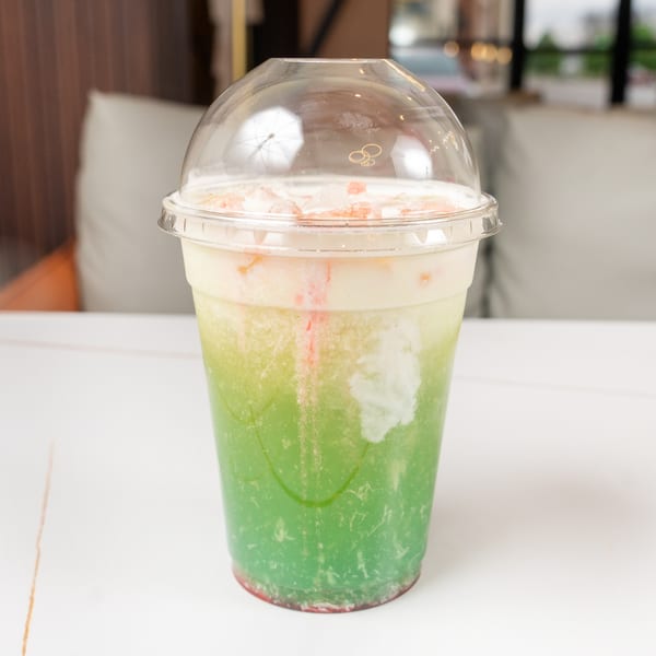A vibrant green and white layered drink with red syrup and ice in a clear plastic cup.