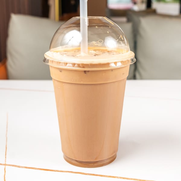 Iced coffee in a plastic cup with a dome lid and straw on a white table.