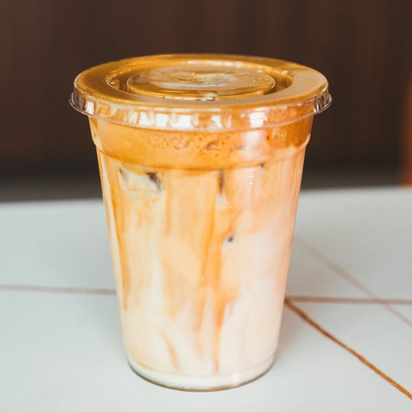 Iced coffee with milk and a golden foam topping in a clear plastic cup.