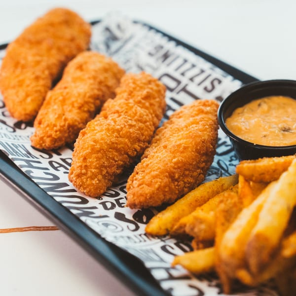 Crispy fried chicken tenders, golden french fries, and a side of dipping sauce on a tray.