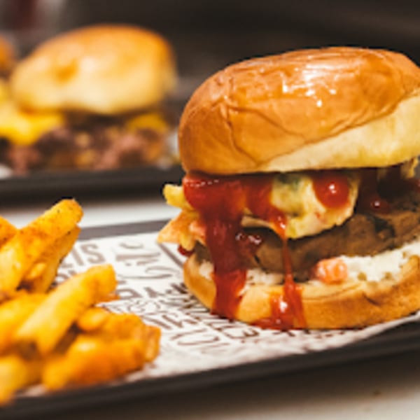 A close-up of a burger with ketchup and fries on a patterned paper-lined tray.