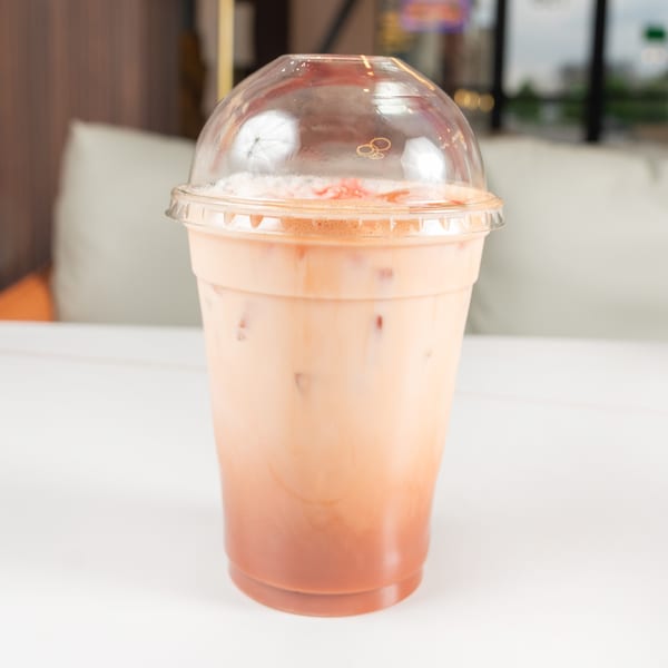 Iced Thai tea with milk and ice in a clear plastic cup with a dome lid.