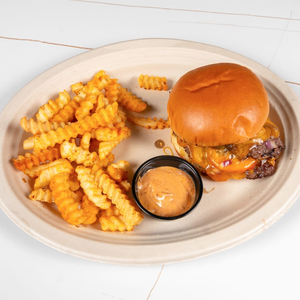Cheeseburger with crinkle-cut fries and a side of dipping sauce on a beige plate.