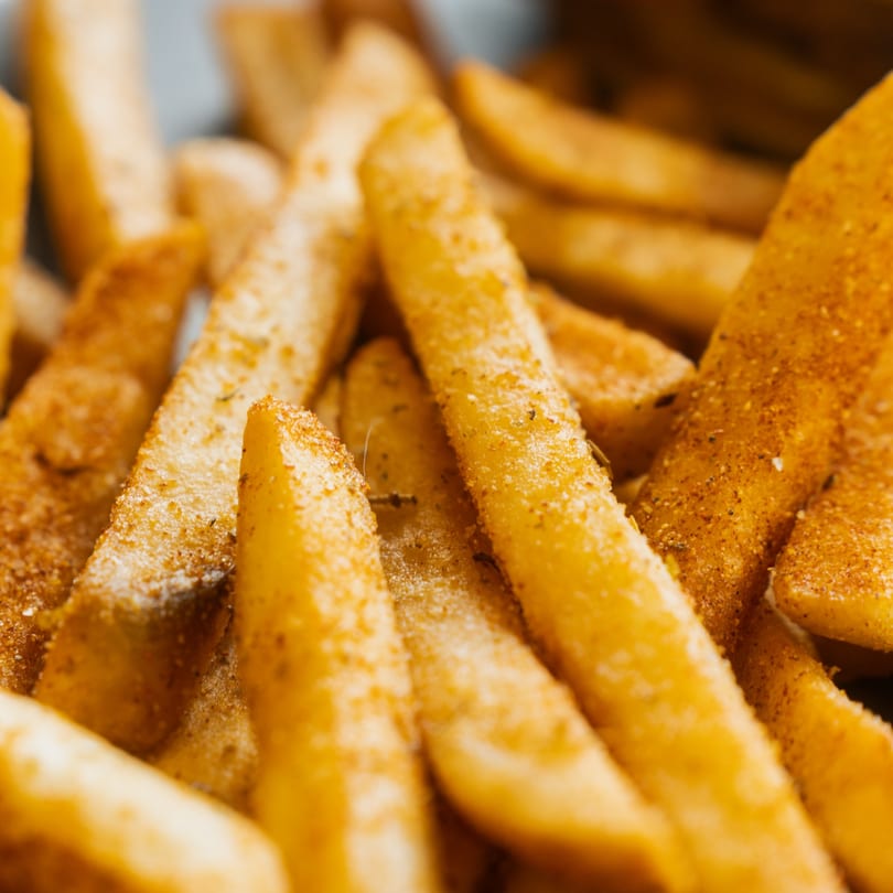 Close-up of golden, seasoned french fries, some with visible salt and spice.