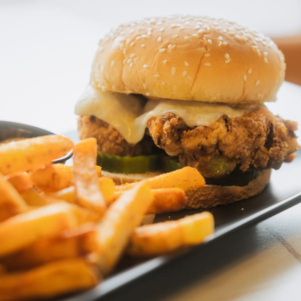 Crispy fried chicken sandwich with melted cheese and pickles, served with golden french fries.