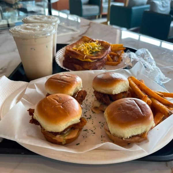 A tray with four chicken sliders, fries, a grilled cheese sandwich, and two iced drinks.
